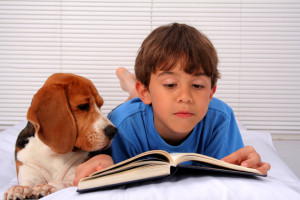 Kid with his dog reading a book in bed
